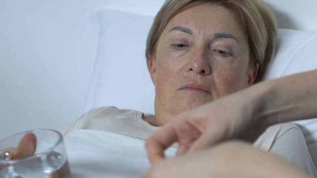 Hospital volunteer giving female patient medicine with glass of water, treatment