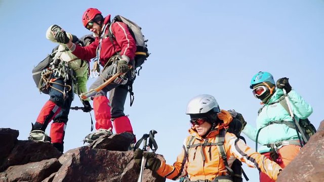 Climbers In Equipment Slowly Down One After Another From The Rock, Helping Each Other. They Are Dressed With Special Gear, Protective Masks And Mountain Sticks.