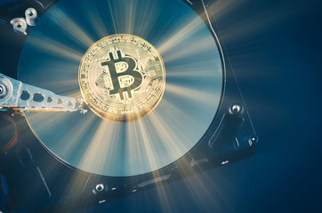 Virtual Cryptocurrency and Blockchain Technology concept, golden bitcoin on dismantle hard disk over gently lit dark background and light ray
