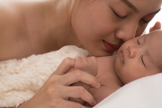 pretty happy young asian mom holding and kiss her newborn baby with love and care on white background bed