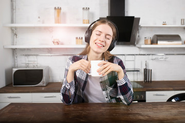 The girl listens to music on headphones and drinks coffee