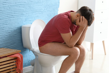 Man suffering from diarrhea while sitting on toilet bowl at home