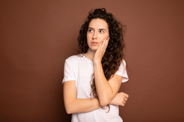 Portrait of an attractive fashionable young brunette woman. Woman thinking. Woman with curly hair on brown background. Emotion portrait