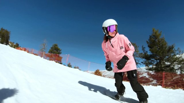 Beautiful young female snowboarder overtakes camera lens on empty wide slope on sunny cold winter day. Apres ski and active lifestyle lover. Millennial adventure seeker
