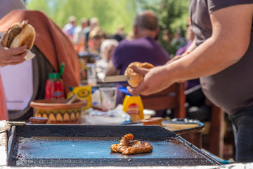 A fat young guy makes hamburgers with fried beef succulent appetizing cutlets and sells them to the guests of the festival