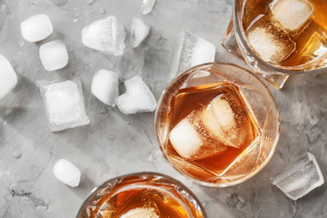 Glasses of cold whiskey with ice on grey background
