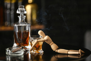 Glass and bottle of cold whiskey with mannequin and cigar on table in bar