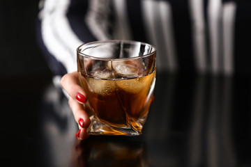 Woman with glass of cold whisky at table in bar, closeup