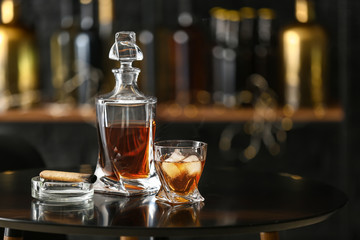 Glass and bottle of cold whiskey with cigar on table in bar