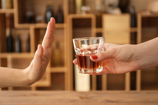 Woman with glass of whiskey and man refusing to drink in bar