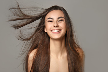 Portrait of beautiful young woman with healthy long hair on grey background