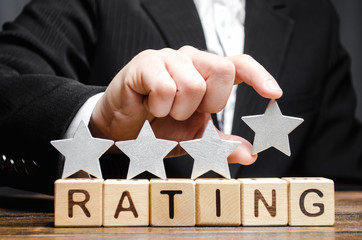 Businessman puts a fourth star above the word Rating on wooden blocks. The concept of the high rating of hotels and restaurants. The evaluation of critics and visitors. Quality level. Four