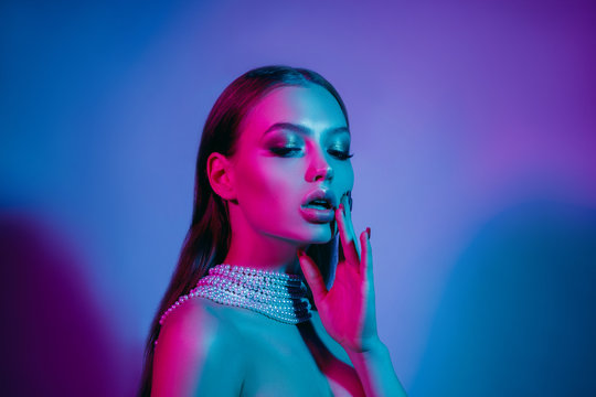 High fashion model in colorful bright neon lights posing at studio. Portrait of beautiful girl with trendy glowing make-up. Art design vivid style.