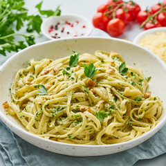 Pesto pasta, bavette with walnuts, parsley, garlic, nuts, olive oil. Side view, close-up, blue background.