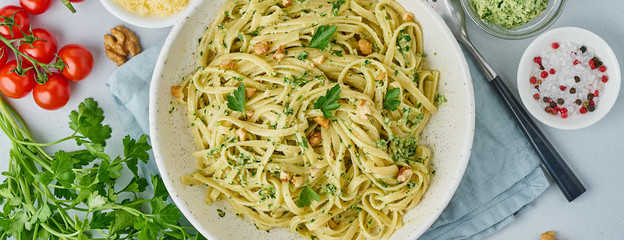 Banner with pesto pasta, bavette with walnuts, parsley, garlic, nuts, olive oil.Top view, long side, blue background.