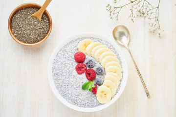 Chia pudding in bowl with fresh berries raspberries, blueberries. Top view, white wooden light background.
