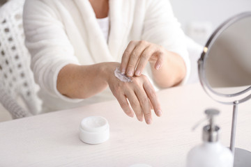 Obraz na płótnie Canvas Mature woman applying hand cream at home