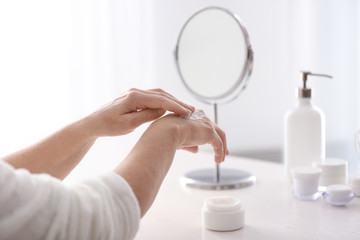 Mature woman applying hand cream at home