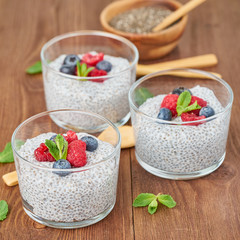 Chia pudding with fresh berries raspberries, blueberries. Side view, three glass on brown wooden background, close up.