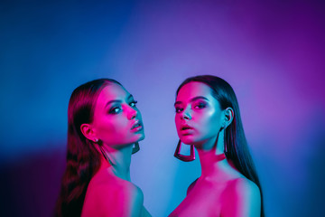 High fashion models in colorful bright neon lights posing at studio. Portrait of beautiful girls with trendy glowing make-up. Art design vivid style.