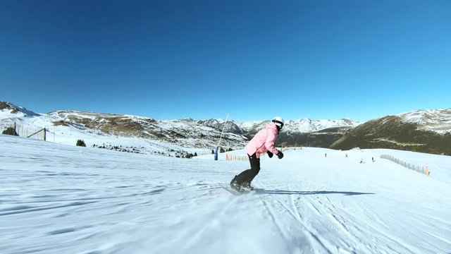 Female snowboarder rides down wide and open fresh snow slope or piste, bright and colorful colors of winter vacation weekend getaway. Healthy sports in outdoors and extreme activity
