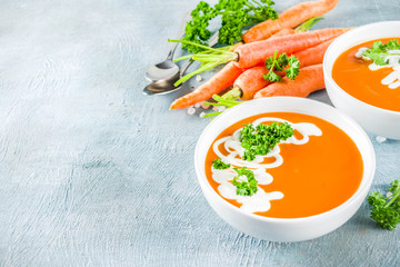 Spring vegetable soup. Homemade carrot cream soup, with fresh organic carrots, sour cream and herbs, blue concrete background copy space