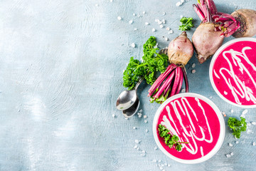 Spring vegetable soup. Homemade beet cream soup, with fresh organic beetroot, sour cream and herbs, blue concrete background copy space