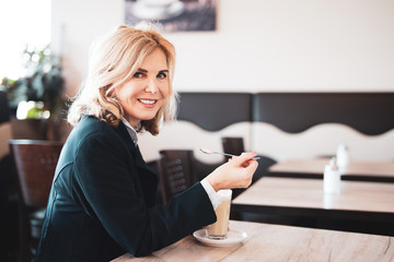 Frau trinkt einen Kaffee in einem Cafe und lächelt in die Kamera 