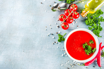 Spring vegetable soup. Homemade tomato cream soup, with fresh organic tomatoes and chili peppers, sour cream and herbs, blue concrete background copy space