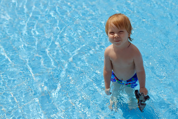 Fototapeta na wymiar Blond-haired toddler standing in the swimming pool