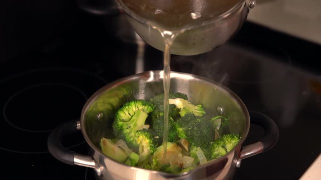 Cook adding seasoned stock to a pot of vegetables