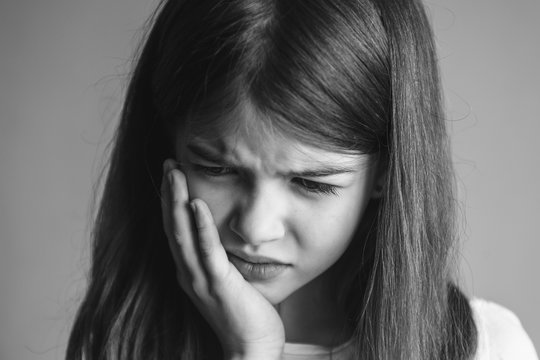 Portrait of a young beautiful girl with toothache, black and white image. Child toothache with sensitive tooth.
