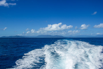 Naklejka na ściany i meble beautiful wake wave behind a big boat for tourist diving at the great barrier reef with blue montains in the background, cairns, australia