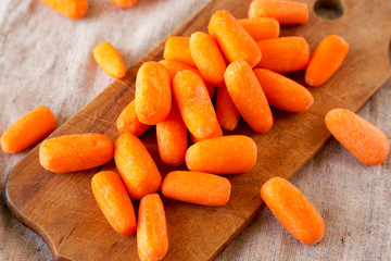 Raw peeled baby carrots on rustic wooden board, side view. Close-up.