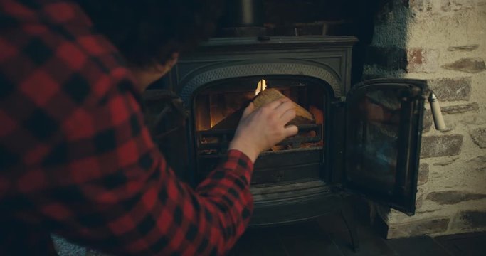 Young man putting logs on fire in logburner