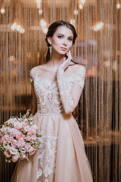 Closeup portrait of a young beautiful woman bride in a beige flesh-colored dress with lace. Interior with lots of lamps, restaurant, vintage armchairs and chairs, dramatic light, fashion style.