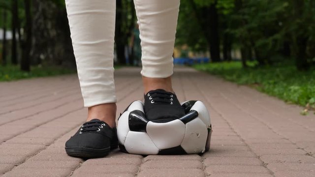 Girl put boot on soccer ball and trump it down, low camera position. Ball deflate and lie squeezed under black shoe. Bad game result or lost round concept