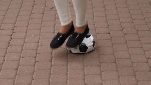 Wicked female player press and jump over to tramp down broken soccer ball, slow motion shot. Girl squeeze down it by foot, then trample and kick away.