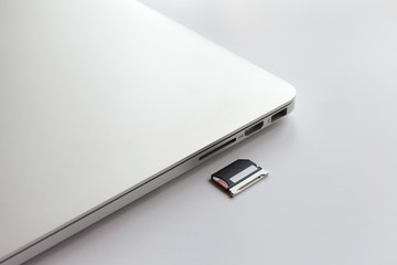 Closed metal laptop on a white table. Near the adapter to the card reader