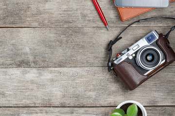 Classic camera on a gray wooden background, with a brown notepad, a red pen, a telephone and green growth. Concept list for a travel photographer