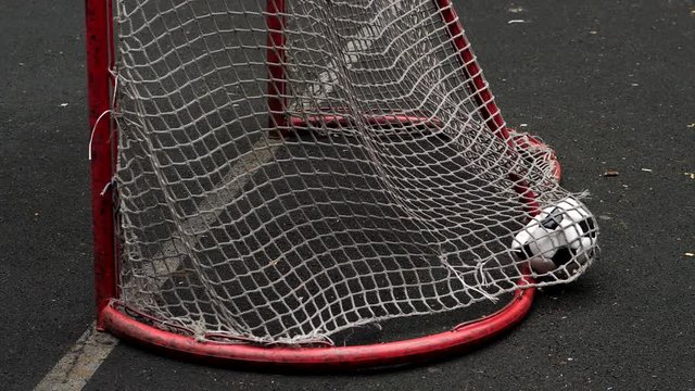 Deflated screwed soccer ball fly into small gate, kick from short distance. Ball hit the net and fall down, slow motion shot from back side. Nobody protecting five-a-side game gate