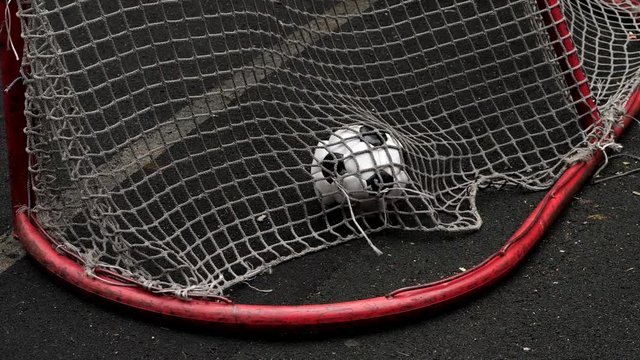 Worn-out and partial deflated soccer ball hit mesh and fall inside small goal gate, slow motion shot from back side. Successful hit in five-a-side game