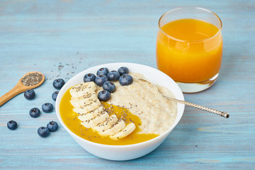 Oatmeal with bananas, blueberries, chia seeds, jam on blue wooden background. Side view. Healthy breakfast.