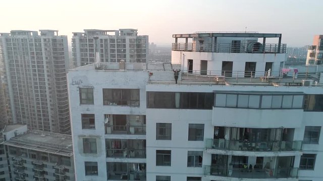 Aerial shot of beautiful european girl waving hands on the edge of roof top of modern apartments building on thee sunset