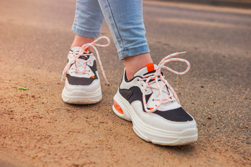 Fototapeta na wymiar Girl in sneakers and jeans. Several pairs of sports shoes and legs. Stylish fashionable white women's leather sneakers on asphalt on a sunny day. Female legs with sneakers