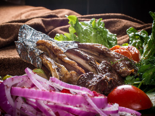 Fried on fire ribs laid out on a wooden Board with vegetables and herbs