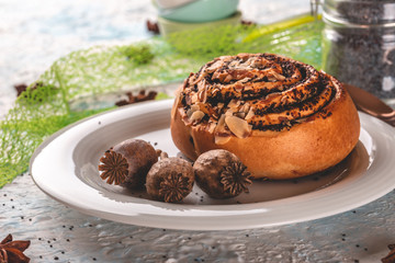 Sweet rolled bun with poppy on white plate with few poppyheads