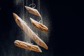 white flour and loaves of fresh baked baguettes on ropes on black background