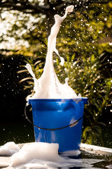 Spring Cleaning outside with big yellow cleaning gloves, water, soap and a big blue bucket with soap. Cleaning the table. Soap Foam on the table. Hands in bucket. Holding and wringing cleaning sponge.