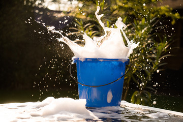 Spring Cleaning outside with big yellow cleaning gloves, water, soap and a big blue bucket with soap. Cleaning the table. Soap Foam on the table. Hands in bucket. Holding and wringing cleaning sponge. © Pepijn